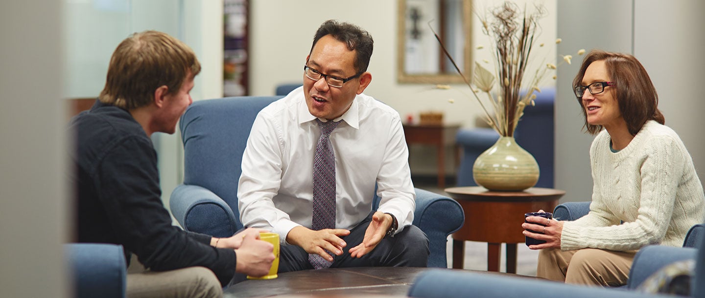 Three Institutional Review Board colleagues sitting at a lounge area on campus having a discussion